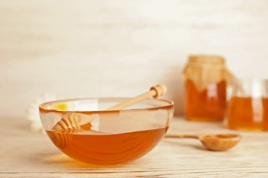 Glass bowl with tasty honey and dipper on wooden table