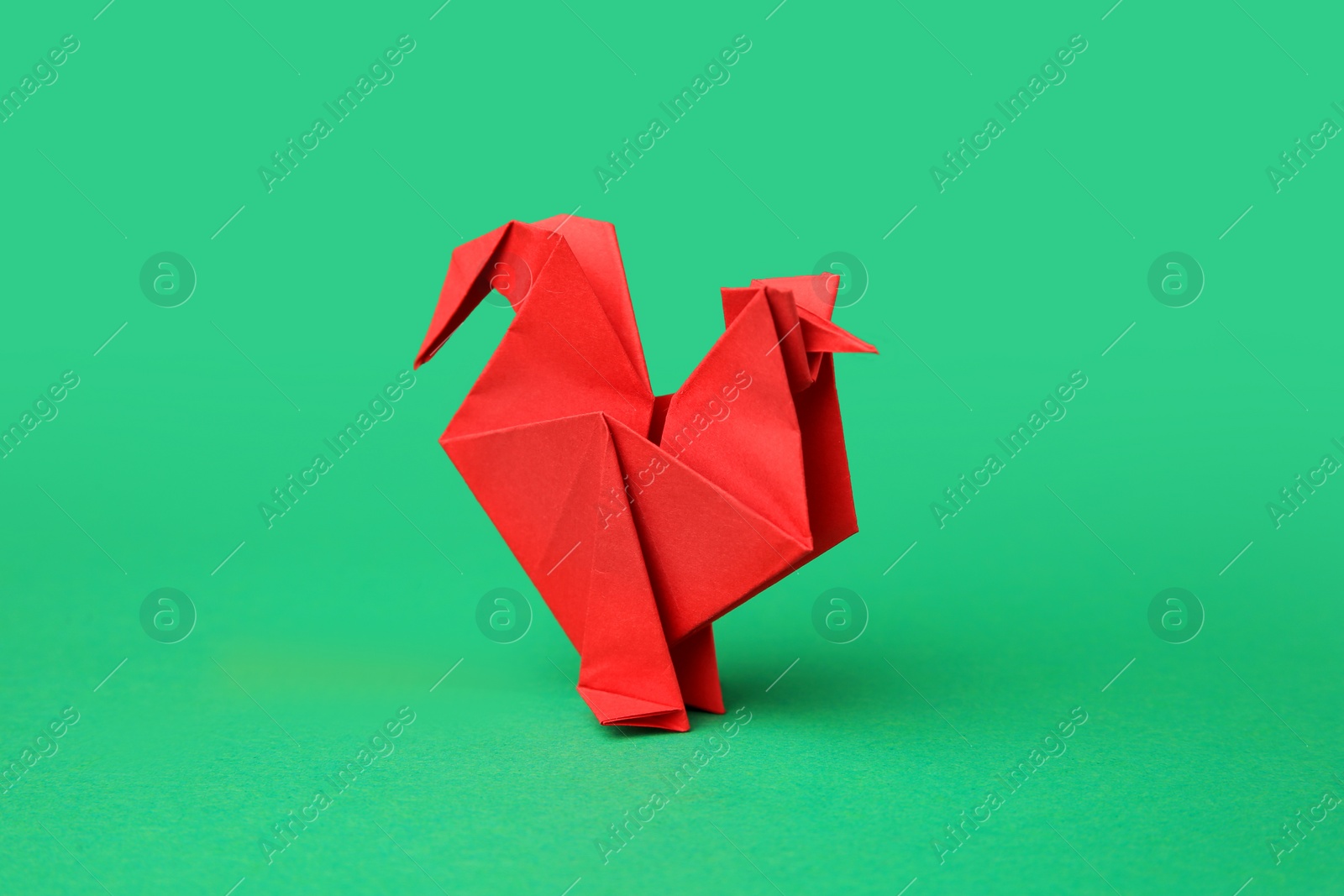 Photo of Origami art. Handmade red paper rooster on green background