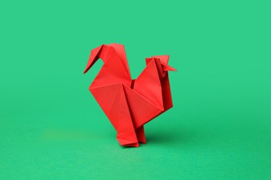 Origami art. Handmade red paper rooster on green background