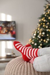 Photo of Woman wearing knitted socks in room decorated for Christmas, closeup