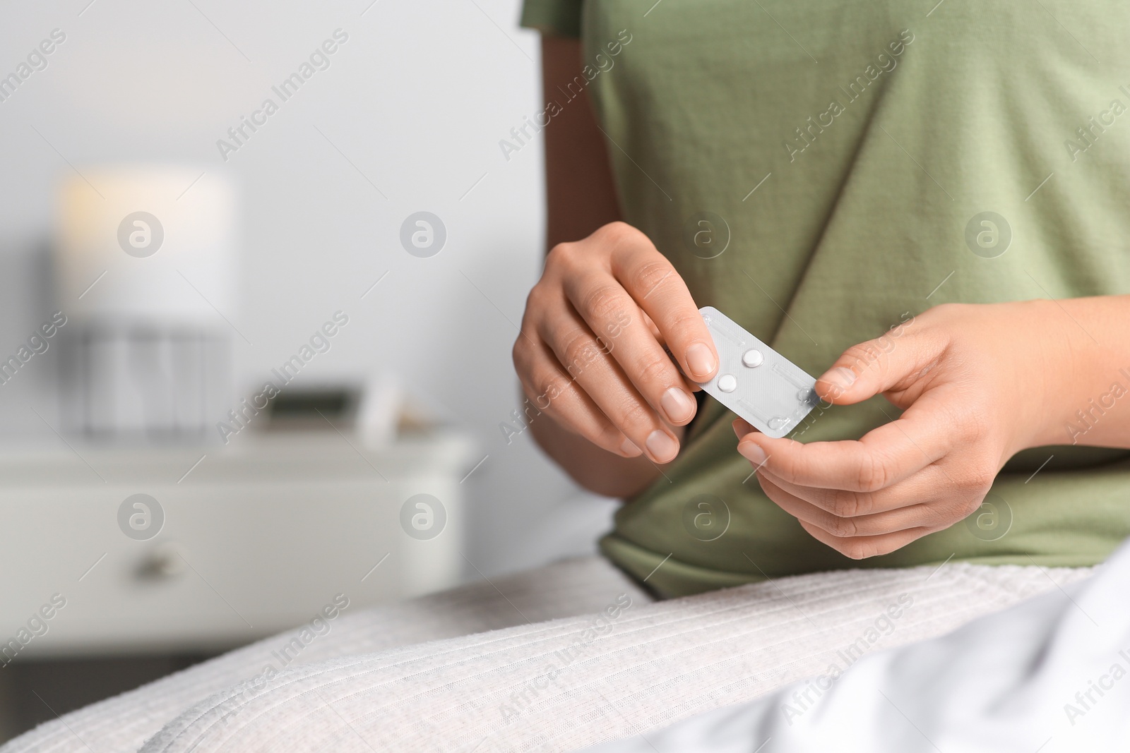 Photo of Woman holding emergency contraception pills in bedroom, focus on hands. Space for text