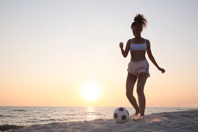Photo of African American woman playing football on beach at sunset. Space for text