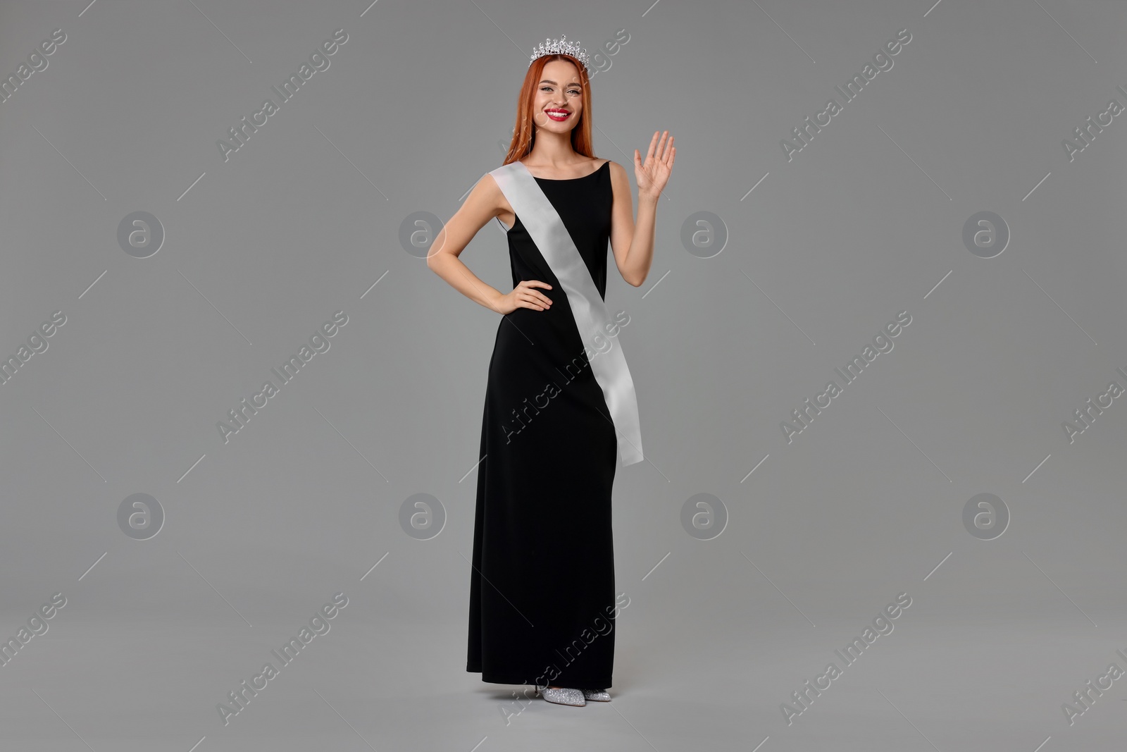 Photo of Beautiful young woman with tiara and ribbon in dress on light grey background. Beauty contest