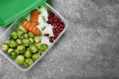 Photo of Tasty rice with cutlets and vegetables in plastic container on grey table, top view. Space for text