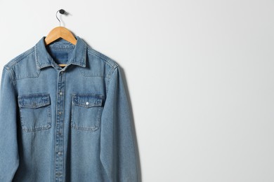 Photo of Hanger with denim shirt on white wall, space for text