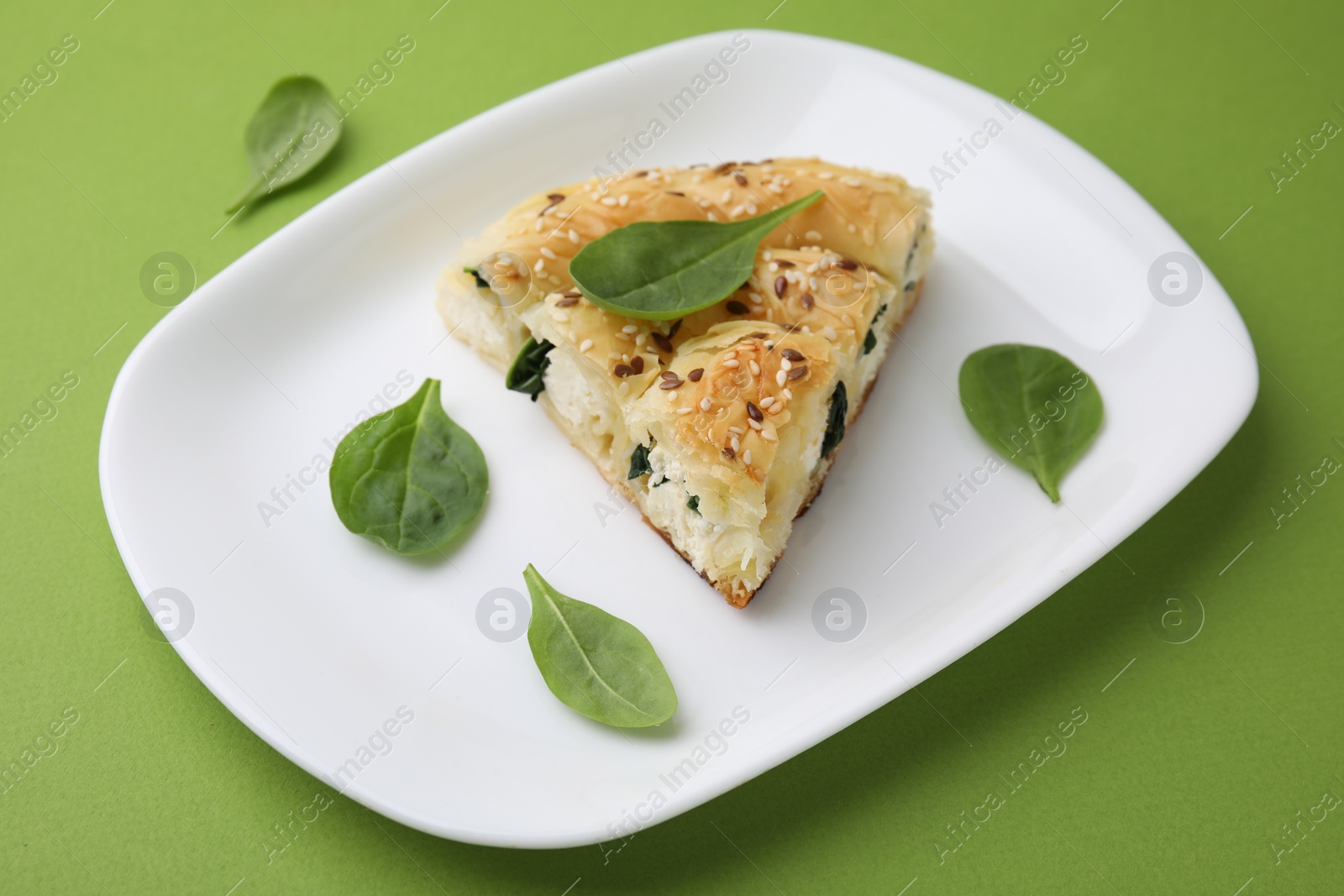 Photo of Piece of delicious puff pastry with spinach on green background