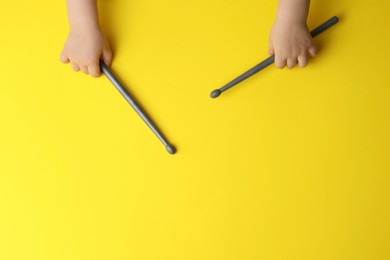 Photo of Little kid holding drumsticks on yellow background, top view. Space for text