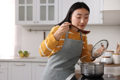 Photo of Beautiful woman cooking and tasting soup in kitchen. Space for text