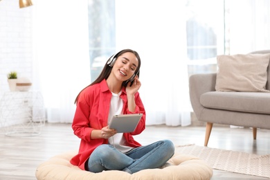 Photo of Young woman with headphones and tablet sitting on floor in living room