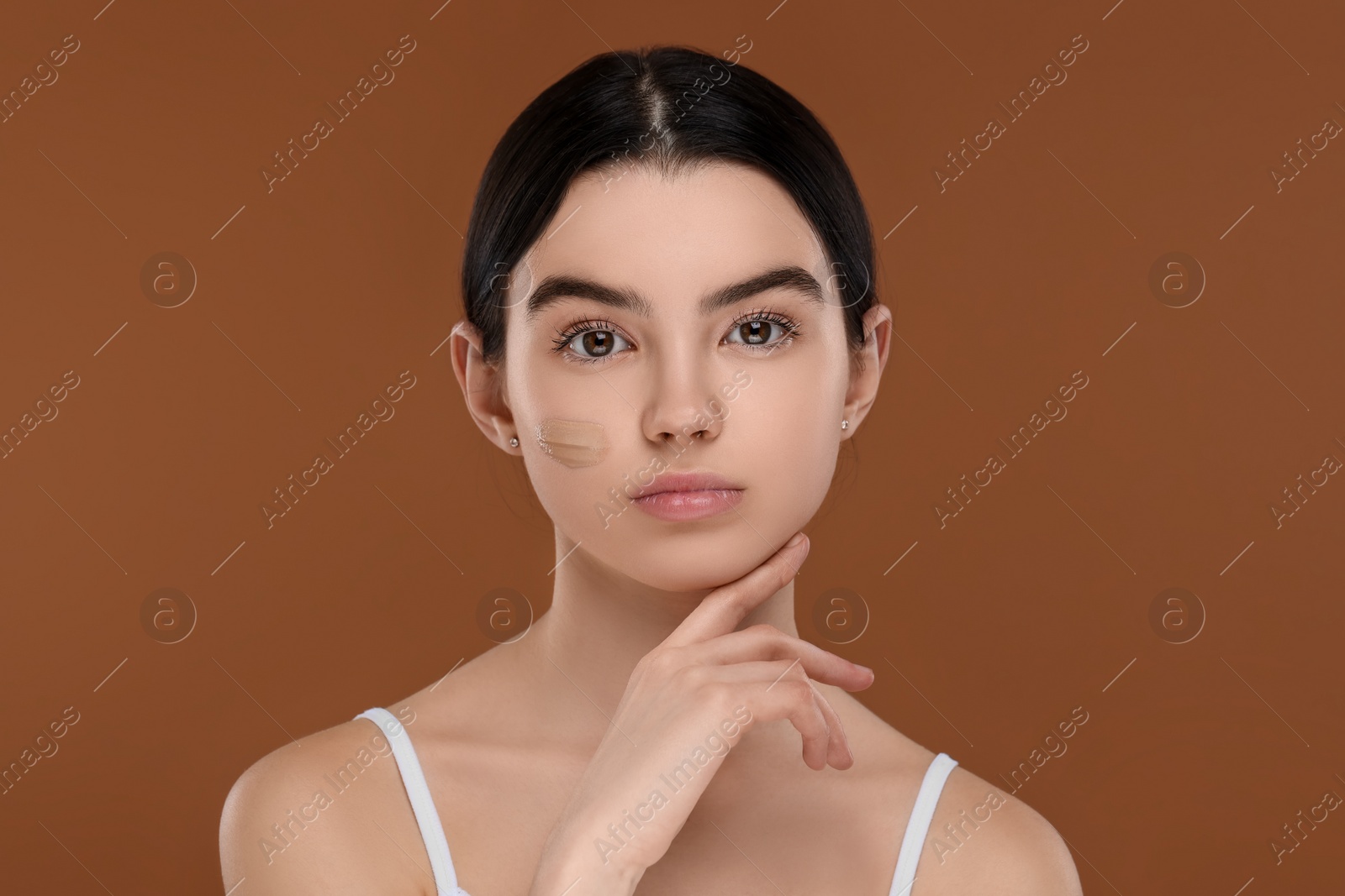 Photo of Teenage girl with swatch of foundation on face against brown background