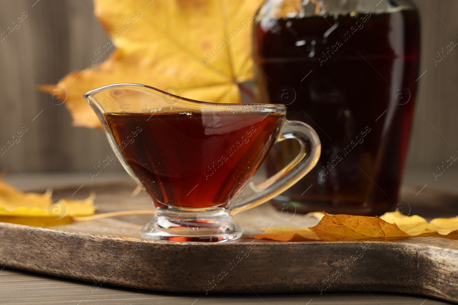 Photo of Gravy boat and bottle of tasty maple syrup on wooden table, closeup