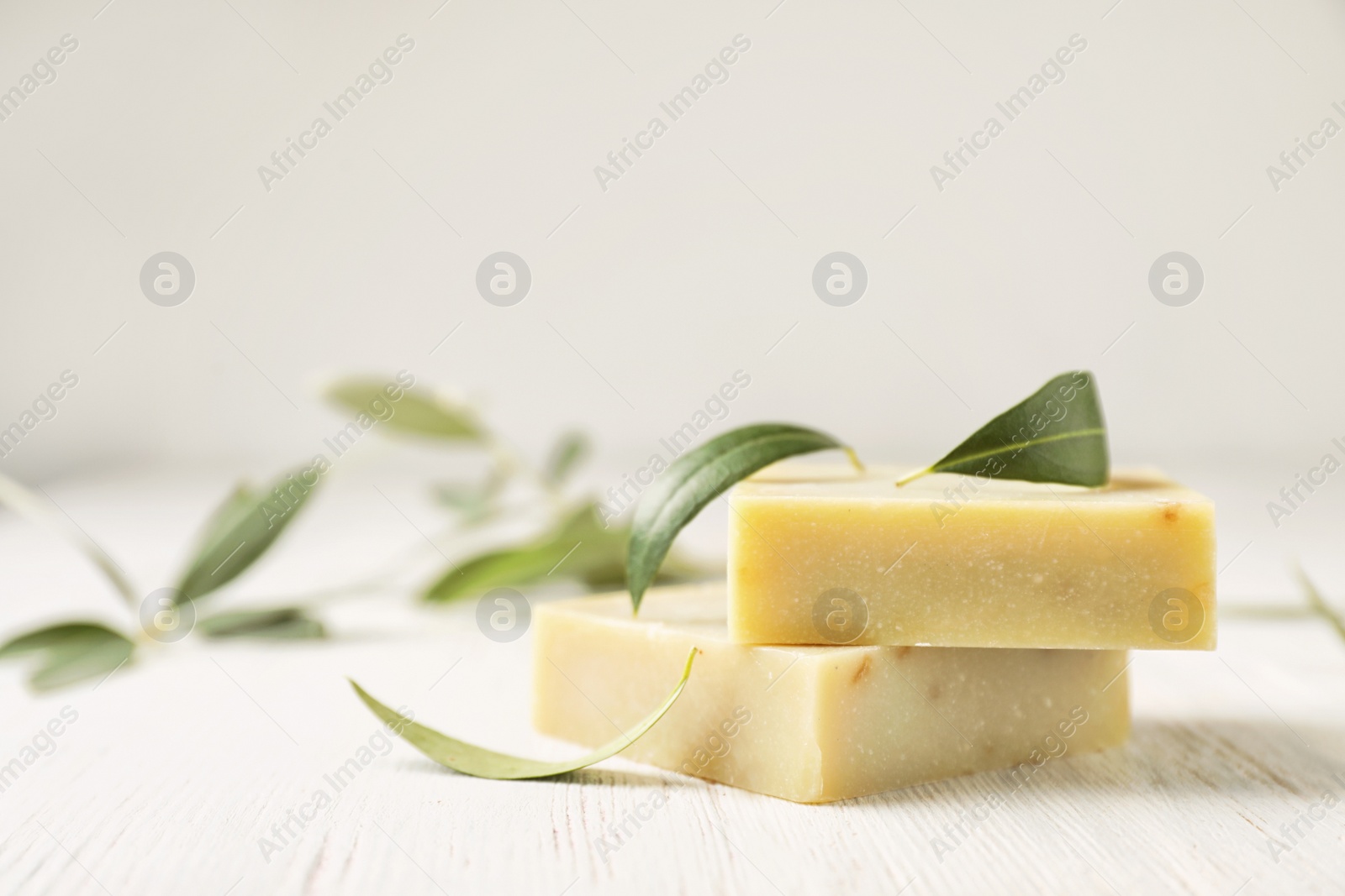 Photo of Handmade soap bars and olive leaves on white table. Space for text