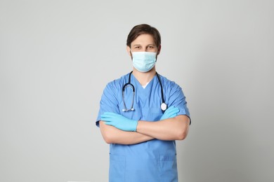 Photo of Doctor or medical assistant (male nurse) with protective mask and stethoscope on light grey background