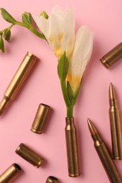 Bullets and cartridge cases with beautiful flower on pink background, flat lay