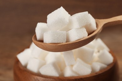 Photo of Wooden spoon with white sugar cubes near bowl, closeup