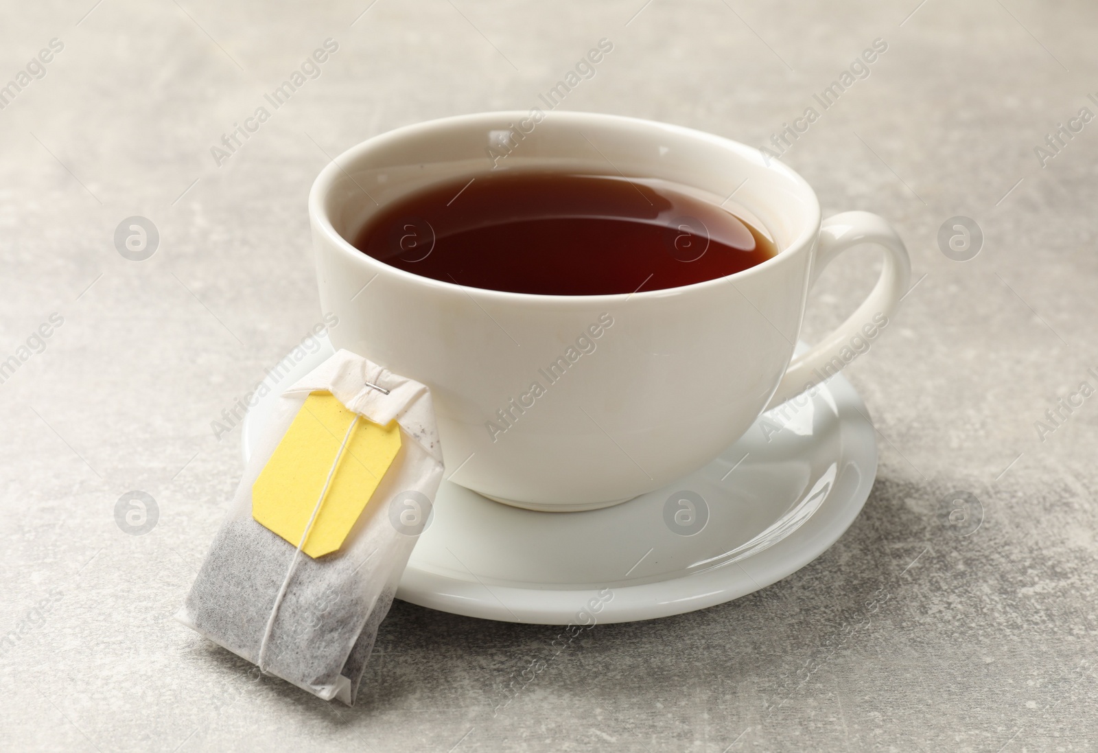 Photo of Tea bag and cup of aromatic drink on grey textured table, closeup