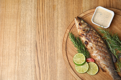 Photo of Delicious grilled fish served on wooden table, top view. Space for text