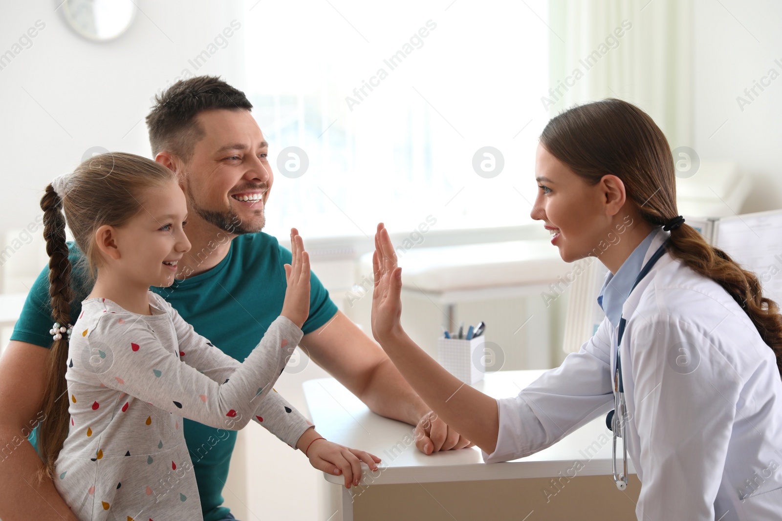 Photo of Father and daughter visiting pediatrician. Doctor working with little patient in hospital