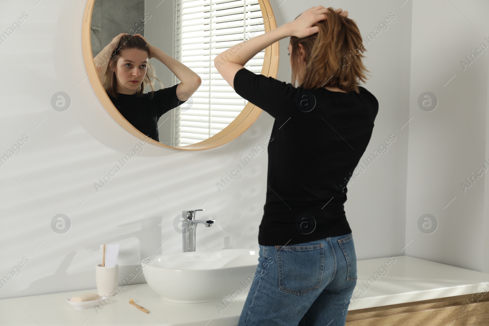 Photo of Sad young woman near mirror in bathroom