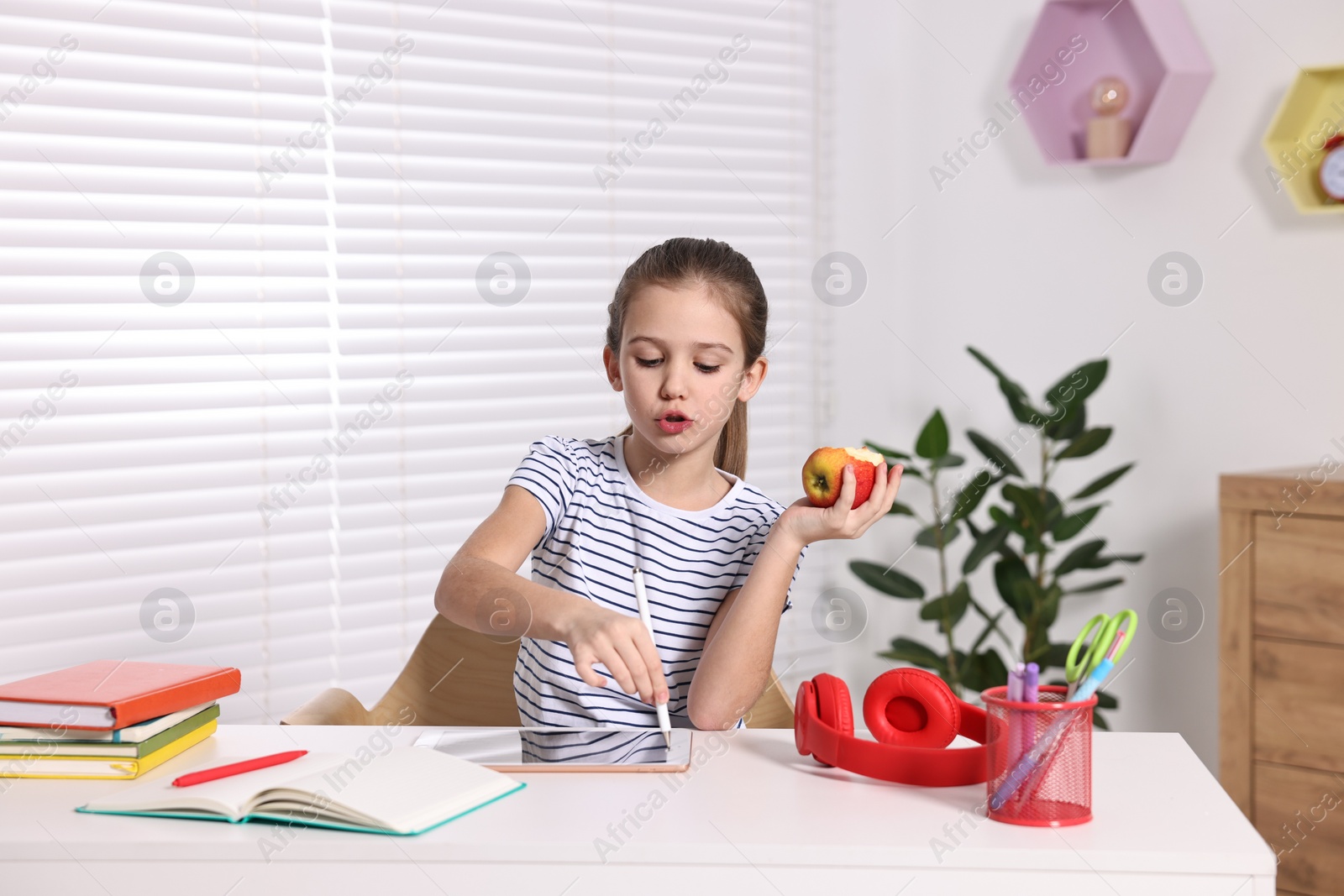 Photo of E-learning. Cute girl with apple using tablet for studying online at table indoors