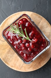 Photo of Fresh cranberry sauce and rosemary in glass bowl on gray textured table, top view