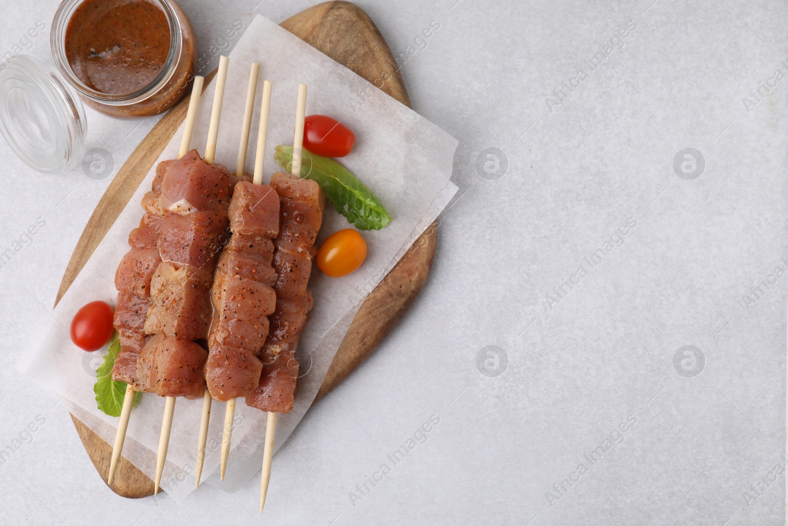 Photo of Wooden skewers with cut raw marinated meat on light grey table, flat lay. Space for text