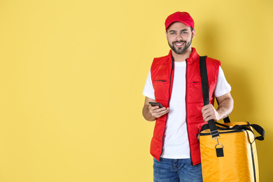 Photo of Courier with thermo bag and mobile phone on yellow background, space for text. Food delivery service