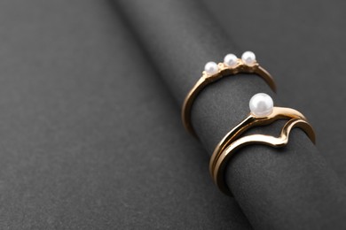 Elegant pearl rings on black background, closeup. Space for text