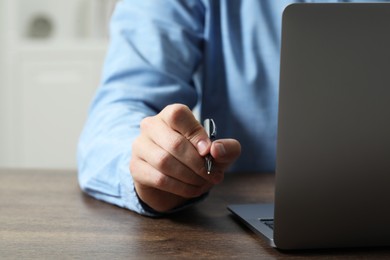 Photo of Man with pen and laptop at wooden table, closeup