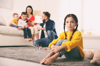 Photo of Unhappy little girl feeling jealous while parents spending time with other children at home