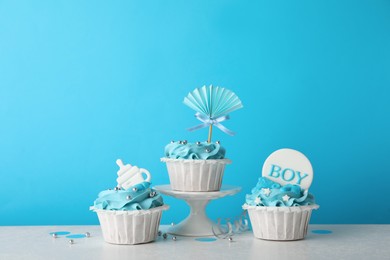 Photo of Baby shower cupcakes with toppers on white table against light blue background
