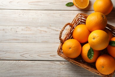 Photo of Many ripe oranges and green leaves on wooden table, top view. Space for text