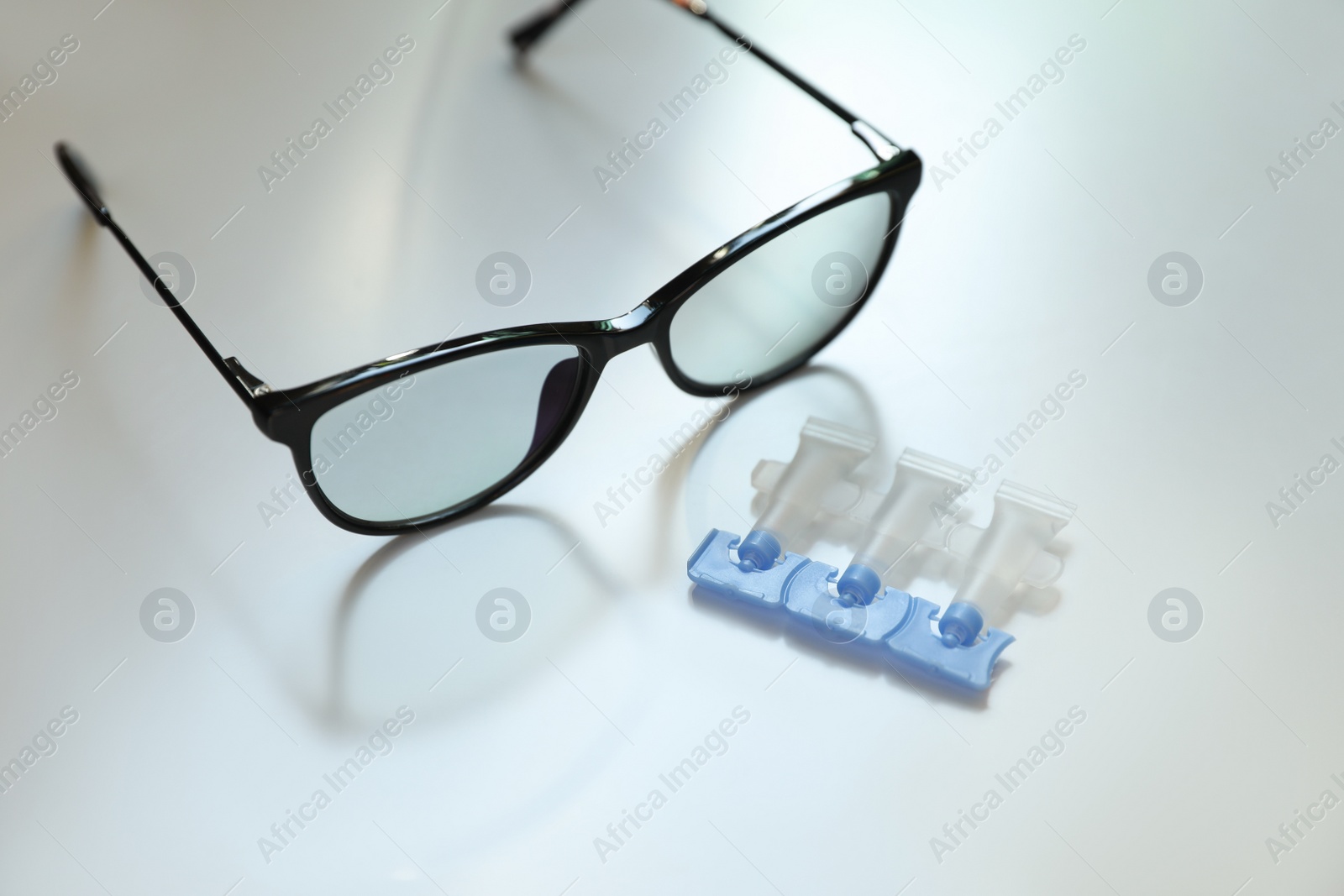 Photo of Single dose eye drops and glasses on white table