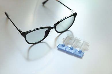 Photo of Single dose eye drops and glasses on white table