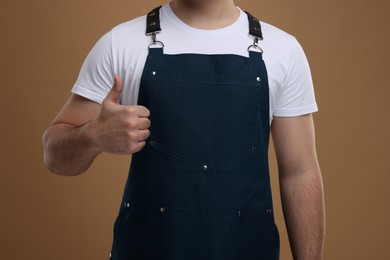 Photo of Man in kitchen apron showing thumb up on brown background, closeup. Mockup for design