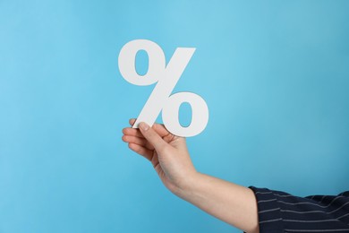 Woman holding percent sign on light blue background, closeup