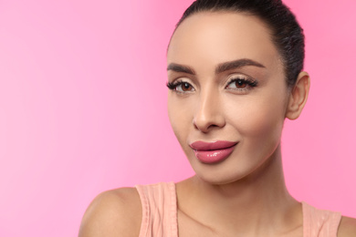Beautiful woman with glossy lipstick on pink background