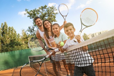 Photo of Happy family with tennis rackets on court outdoors