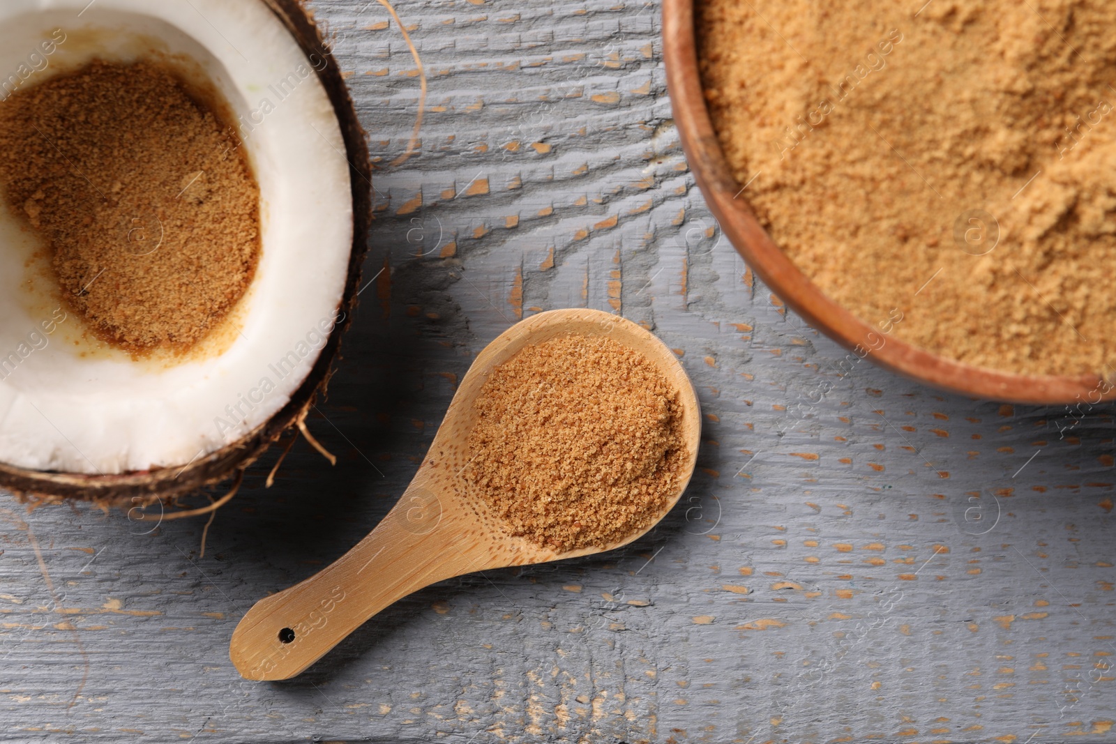 Photo of Coconut sugar, bowl, spoon and fruit on grey wooden table, flat lay