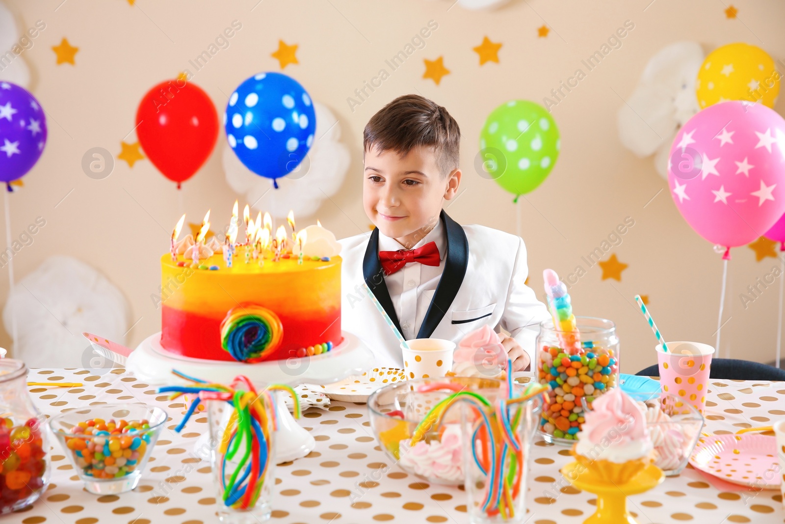 Photo of Cute little boy near table with treats at birthday party indoors