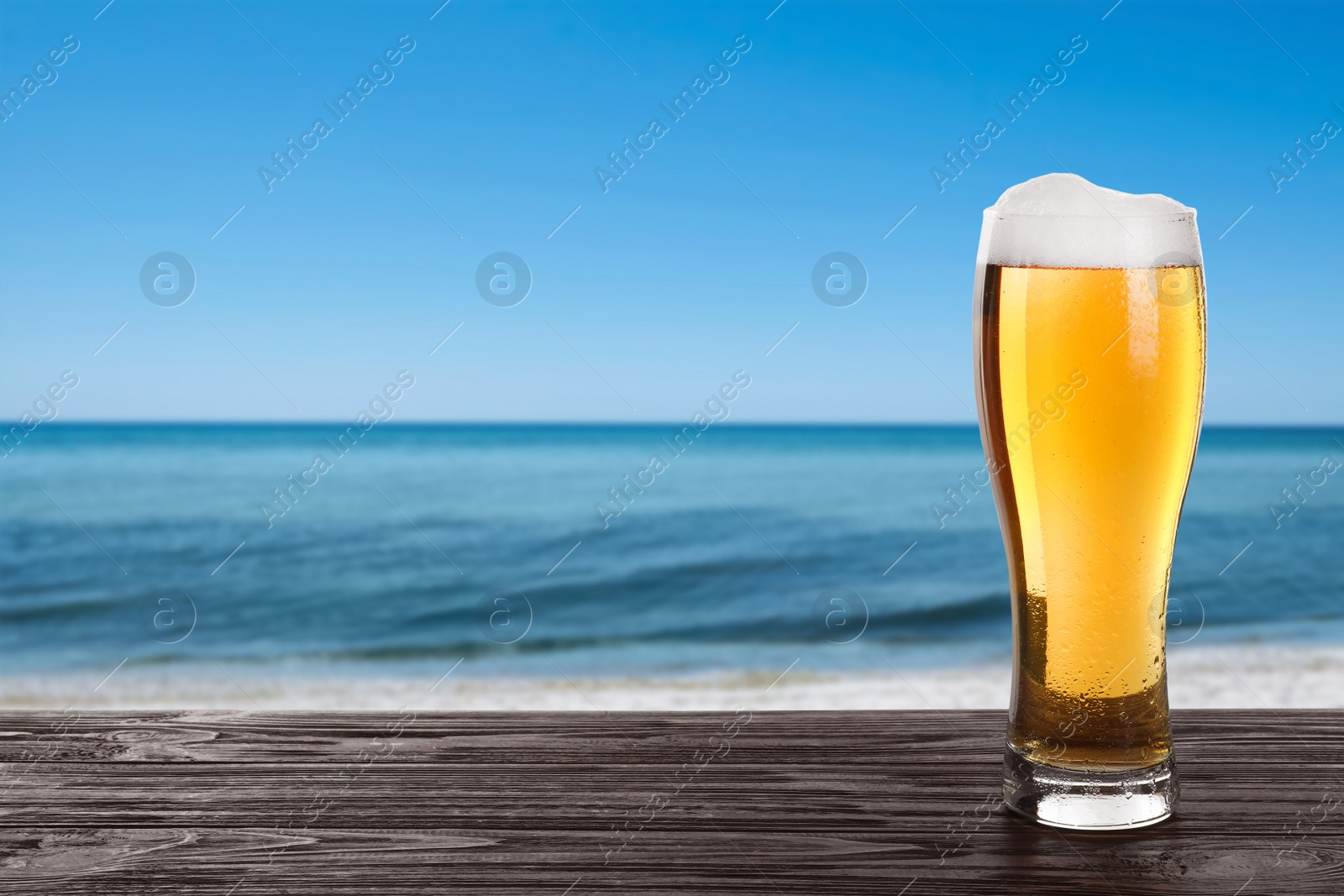 Image of Cold beer on wooden desk against blurred sea. Space for text