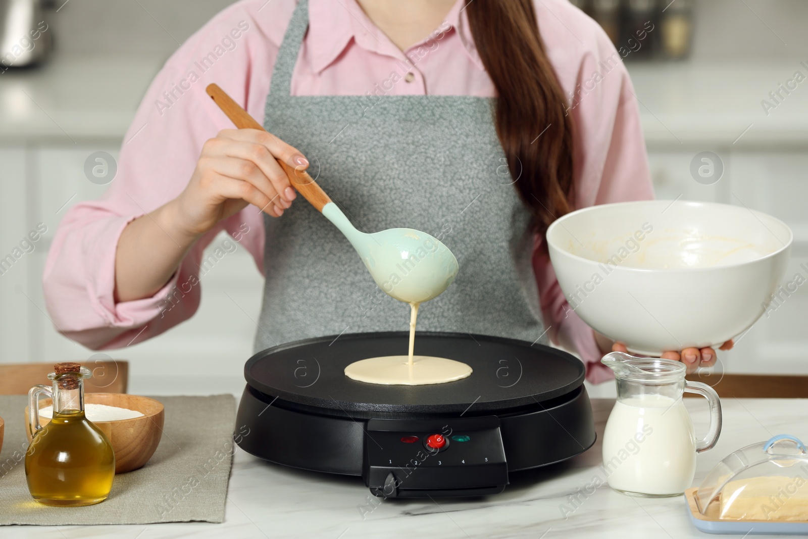 Photo of Woman cooking delicious crepe on electric maker at white marble table in kitchen, closeup