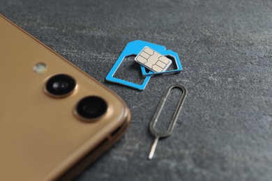 Photo of SIM card, mobile phone and ejector tool on grey table, closeup