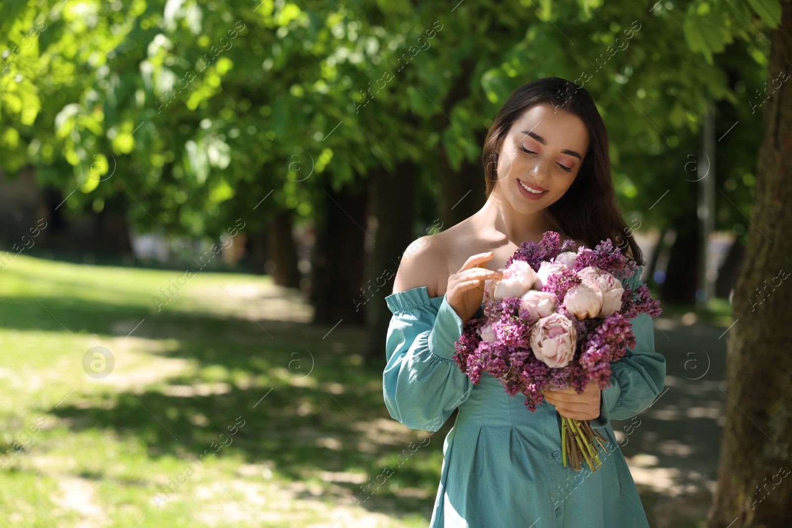 Photo of Beautiful woman with bouquet of spring flowers in park on sunny day, space for text