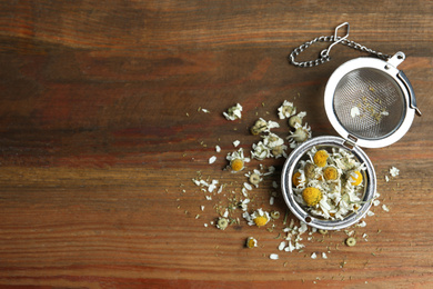 Photo of Dry chamomile flowers in infuser on wooden table, flat lay. Space for text