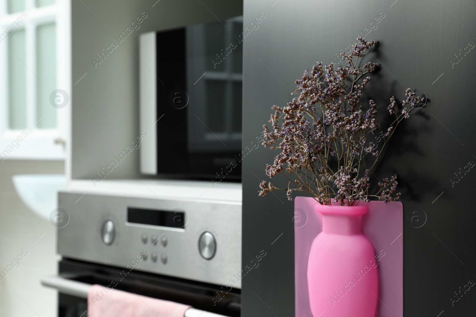 Photo of Silicone vase with beautiful violet flowers on fridge in kitchen, space for text