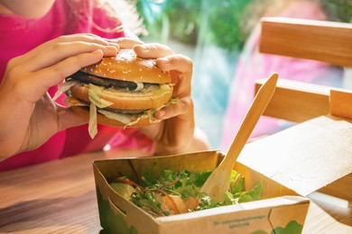 WARSAW, POLAND - SEPTEMBER 16, 2022: Woman with McDonald's burger at table in cafe, closeup