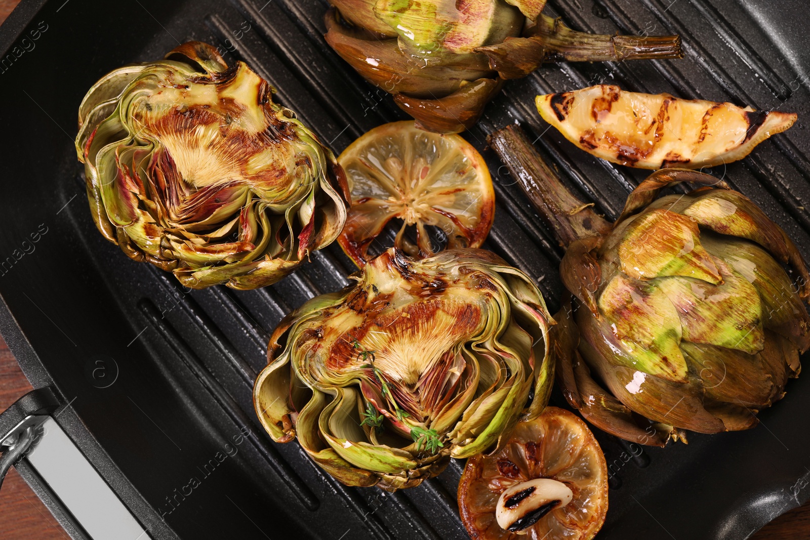 Photo of Tasty grilled artichokes and lemon slice on pan, top view