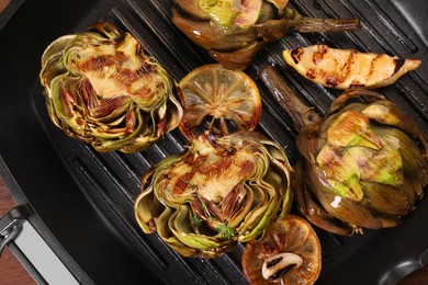 Photo of Tasty grilled artichokes and lemon slice on pan, top view