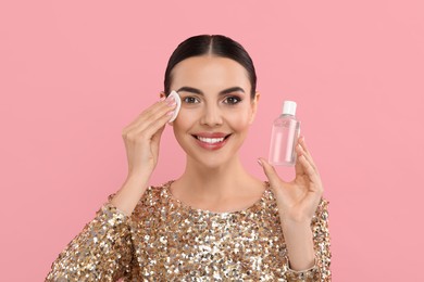 Beautiful woman removing makeup with cotton pad on pink background